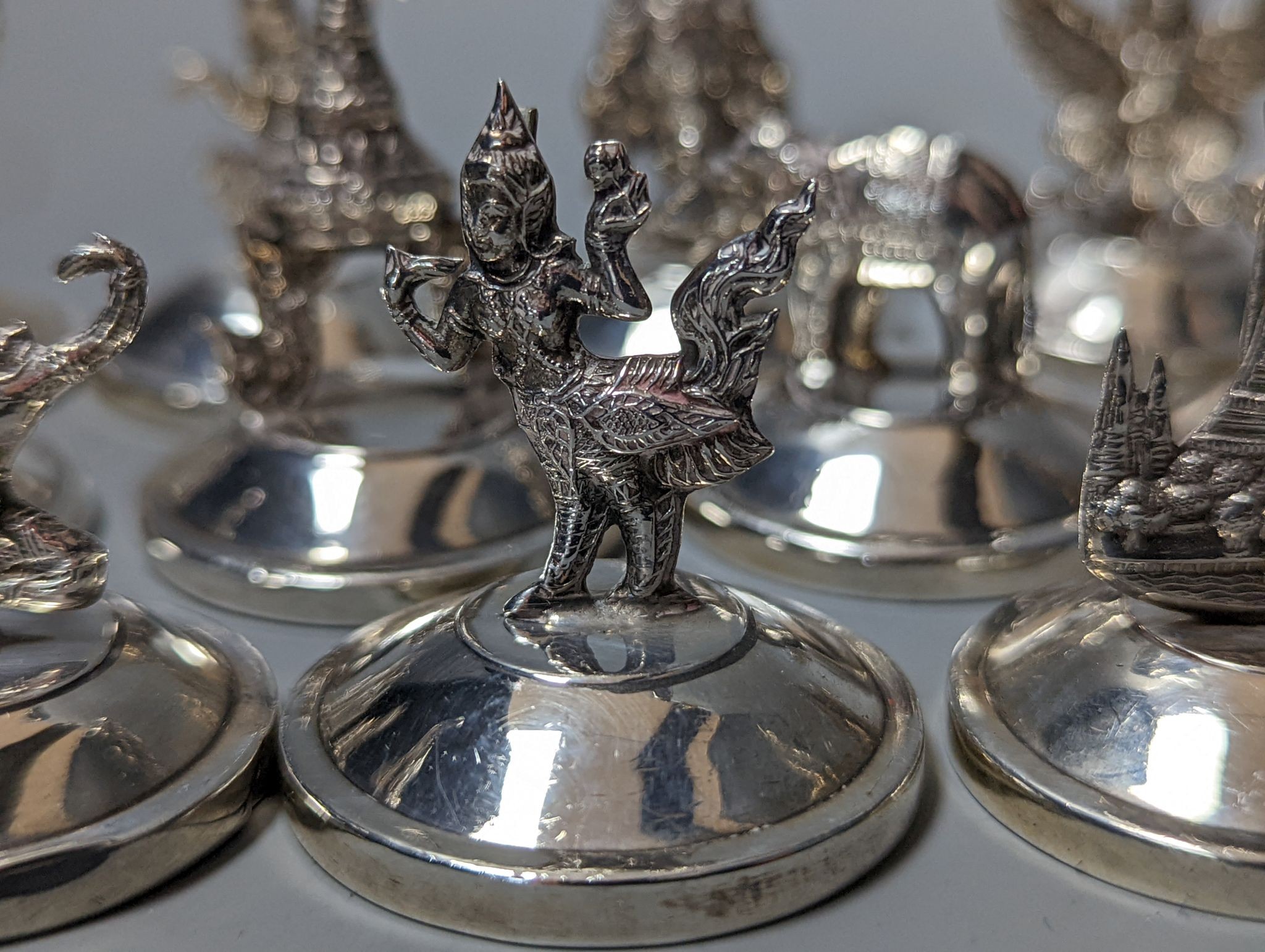 Sixteen assorted Siamese sterling mounted menu holders, modelled with figures, elephant, etc.